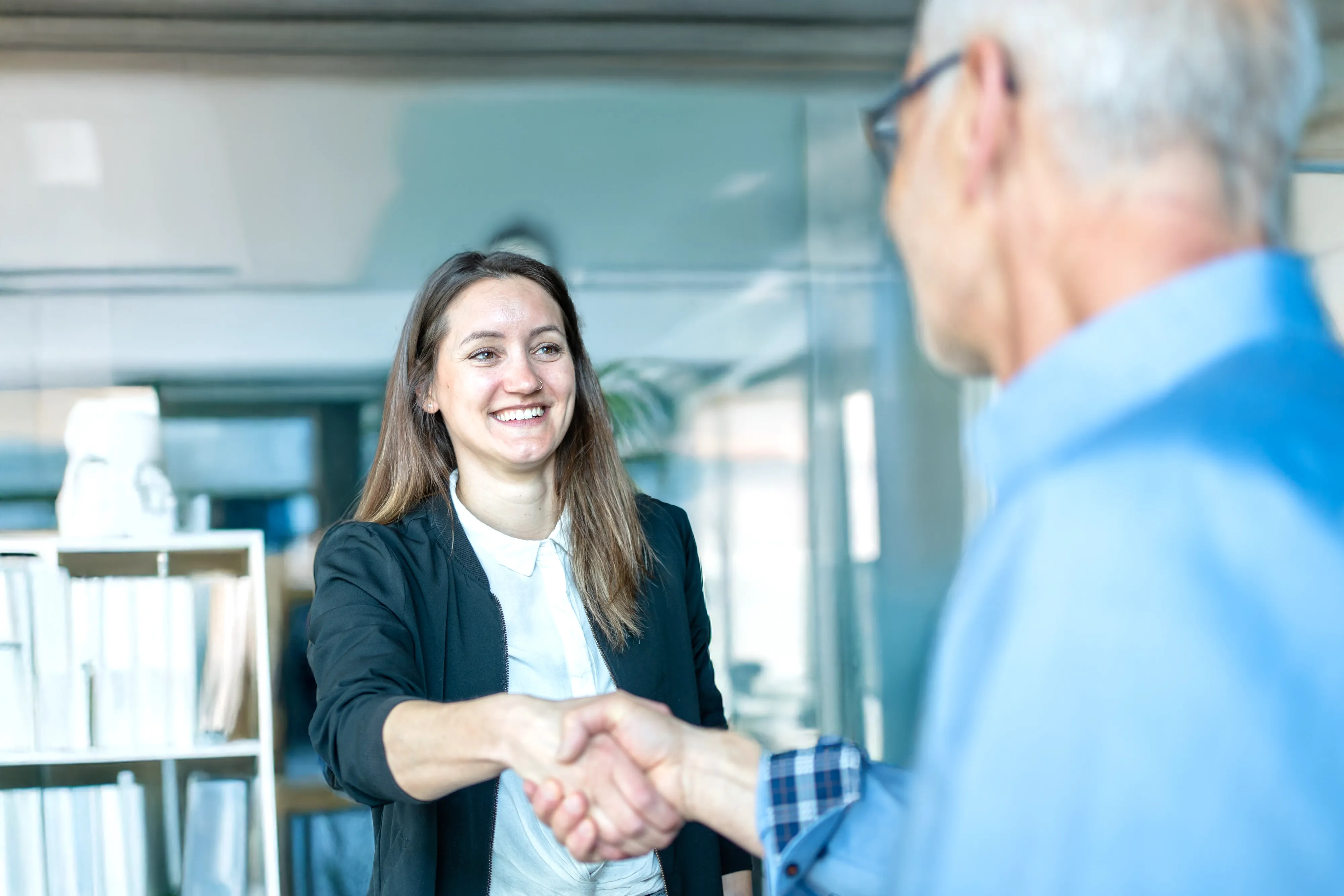 A smiling woman shaking hands with an older man in an office 